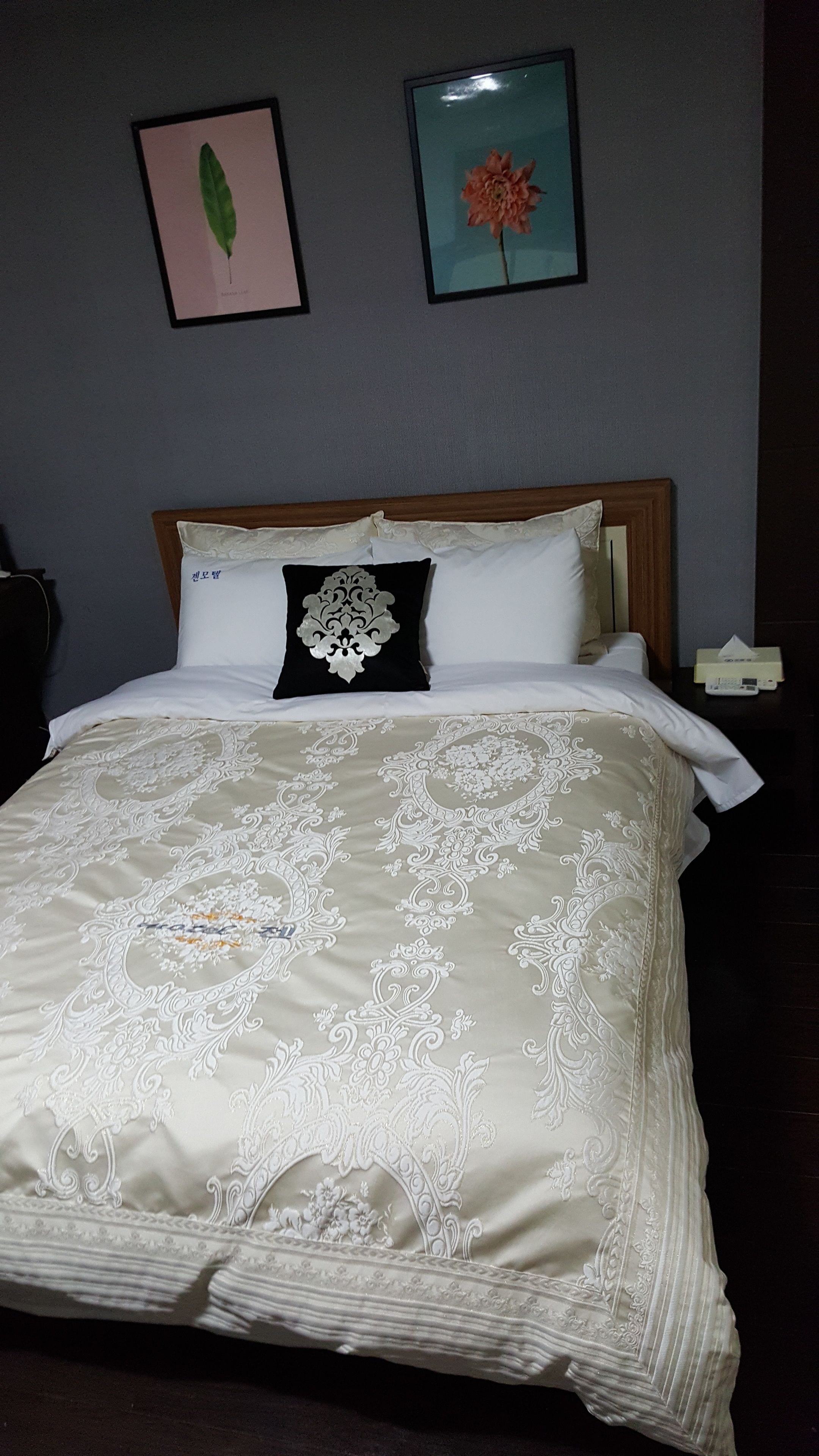 A neatly made bed with a floral-patterned bedspread, a black and white decorative pillow, and two framed floral pictures on the wall.