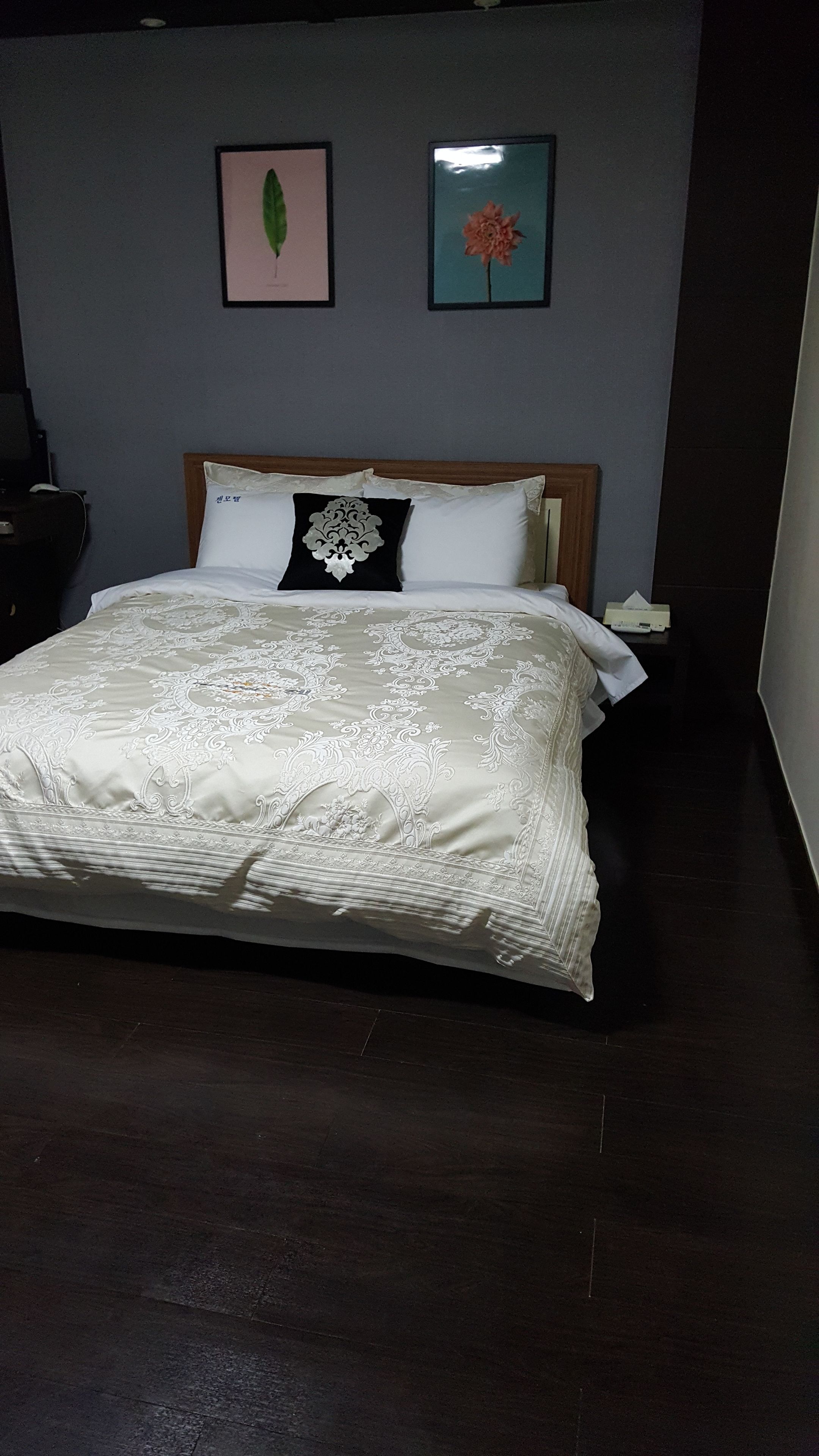Een opgemaakt bed met een bedsprei met dessin, een houten hoofdbord en twee ingelijste foto's aan de muur.