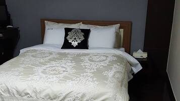 Een opgemaakt bed met een bedsprei met dessin, een houten hoofdbord en twee ingelijste foto's aan de muur.
