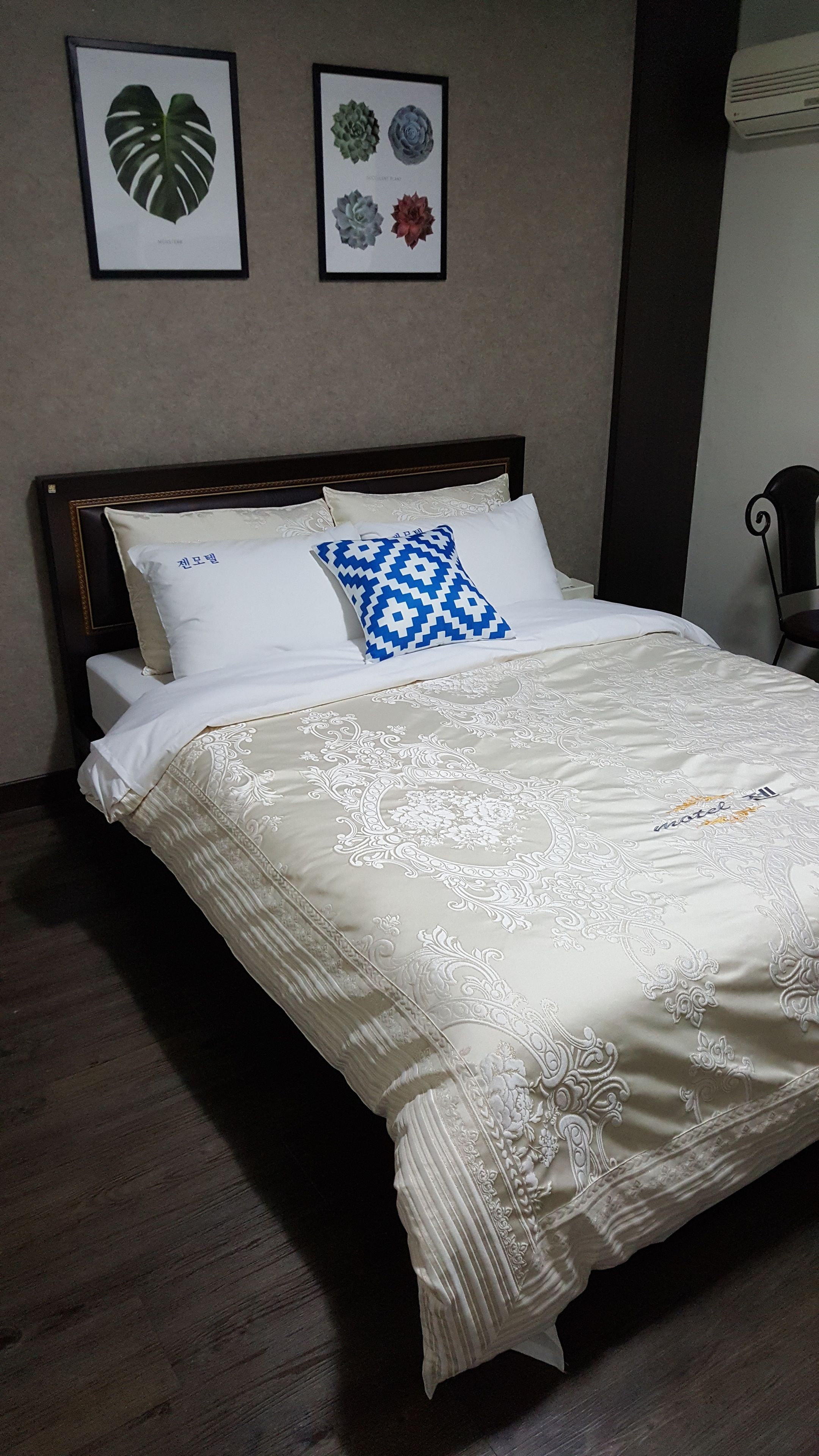 Ein ordentlich gemachtes Bett mit einem gemusterten Bettbezug und Kissen, darunter ein geometrisches blaues Kissen.