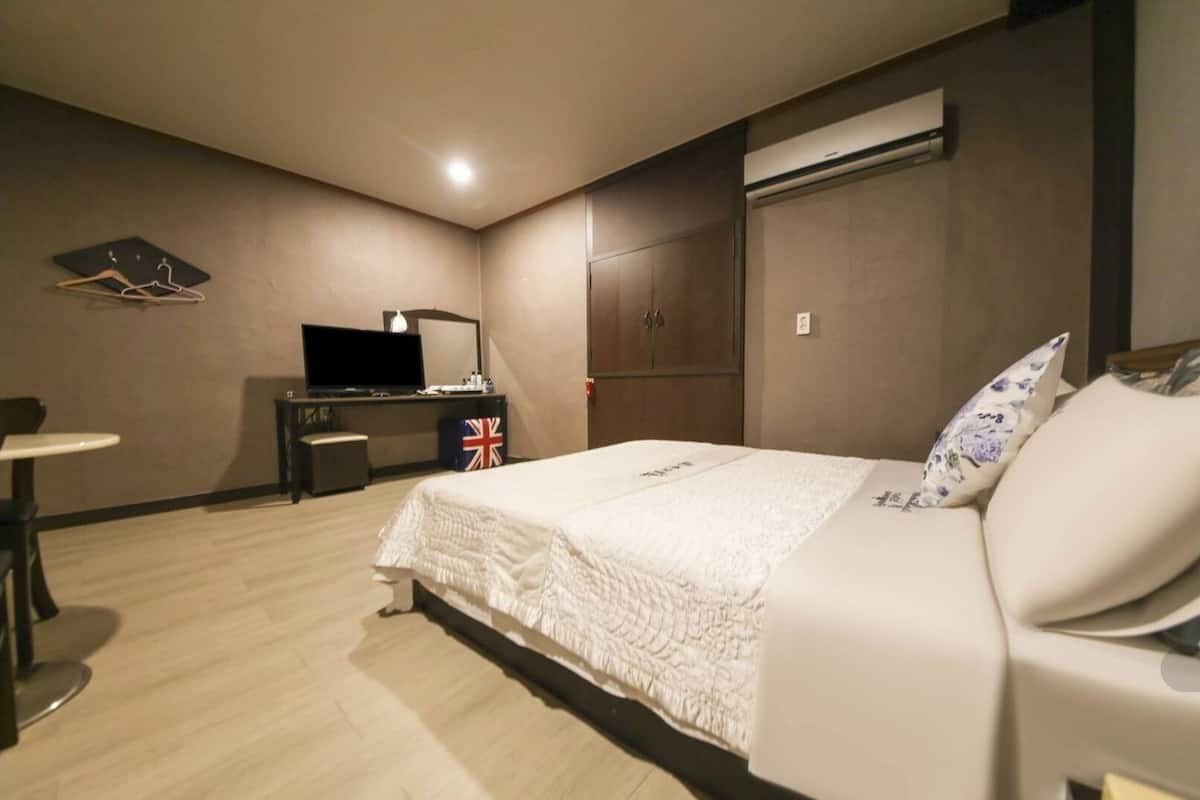Une chambre d’hôtel comprenant un lit, un bureau avec une télévision, une petite table et une armoire.