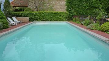 Relax by the pool surrounded by lush greenery and a stone building in the background.