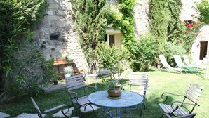 Eine Terrasse mit rundem Tisch und sechs Holzstühlen, umgeben von einer Steinmauer und üppiger Bepflanzung.