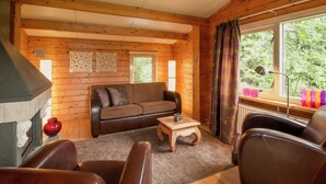 Et hyggeligt sommerhusinteriør med træpaneler, en sofa, et sofabord og et vindue med gardiner.