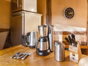 A kitchenette with a microwave, coffee maker, and kettle on a wooden table.