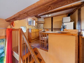 A rustic kitchen with wooden beams, a dining area, and a staircase leading to an outdoor space.
