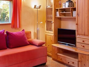 A cozy living room with a red sofa, a flat-screen TV, wooden shelves, and a floor lamp. - Bauernhaus nahe Langlingen Badesee (Langlingen-Hohnebostel)