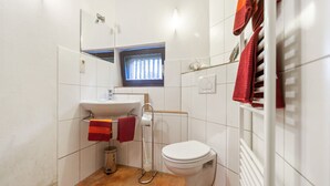 A compact bathroom with a white sink, a toilet, and a shower. There is a window above the sink and a towel rack with towels. - Bauernhaus nahe Langlingen Badesee (Langlingen-Hohnebostel)