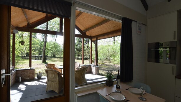 Ein überdachter Essbereich im Freien mit Korbstühlen und einem Steintisch, mit Blick auf einen Garten.