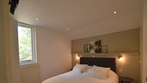 Ein Schlafzimmer mit einem Bett, einem Fenster, einem Heizkörper, einem an der Wand befestigten Regal mit Bildern und einem kleinen Hocker.