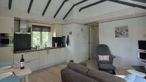 Eine moderne Küche mit weißen Schränken, einem eingebauten Backofen und einem Fenster mit Blick auf Grünflächen. Es gibt einen Essbereich mit Tisch und Stühlen sowie ein graues Sofa.