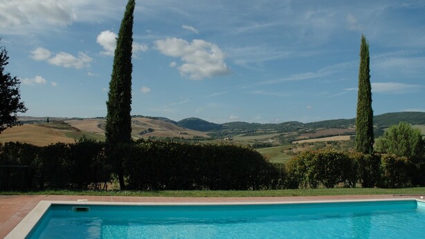 A swimming pool with a view of rolling hills and tall trees in the background. - Spacious house in Pienza (Pienza)