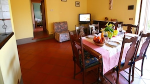 A dining area with a table set for four, chairs, a television, and a floral-patterned armchair. - Spacious house in Pienza (Pienza)