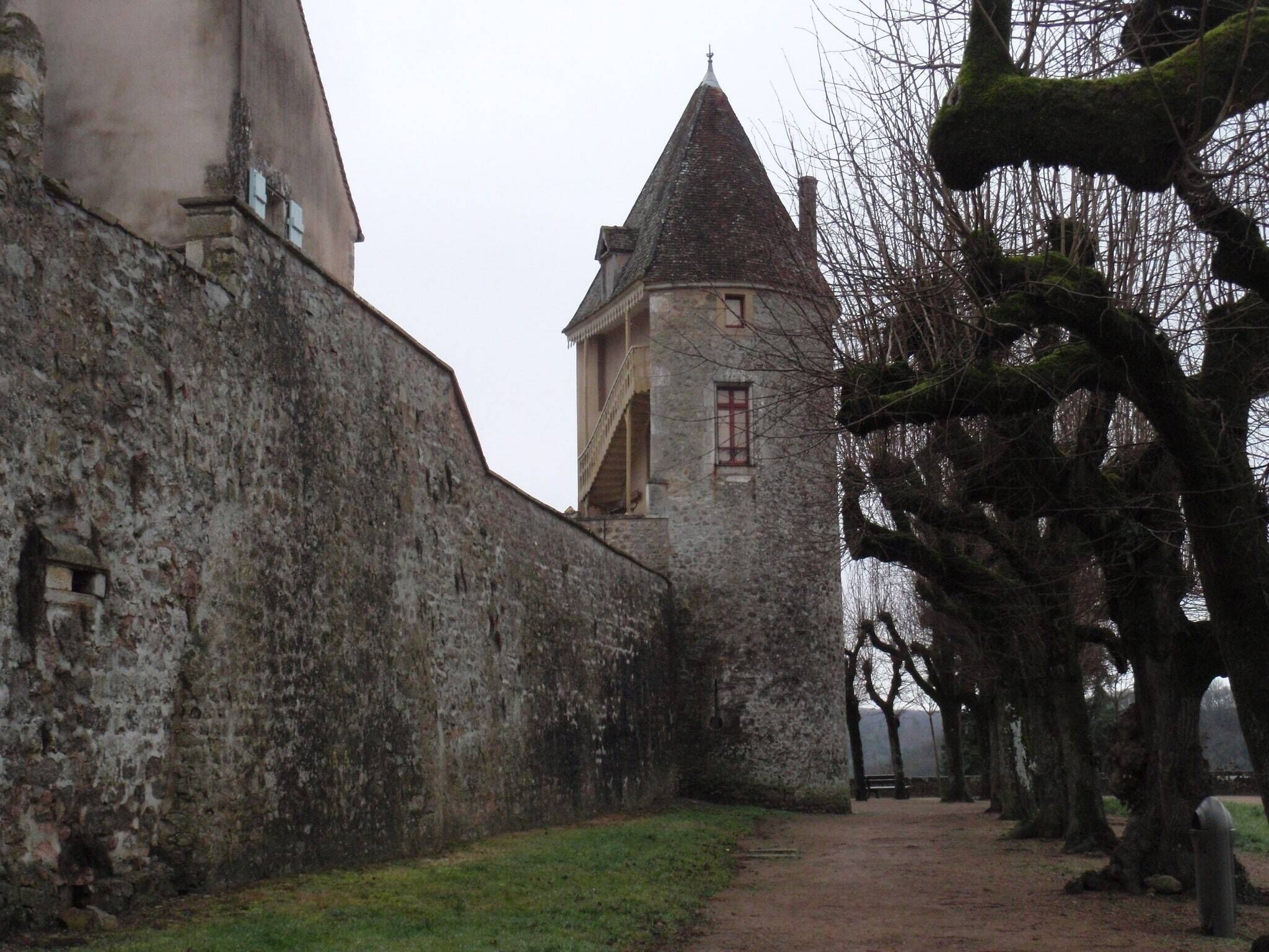 A narrow pathway flanked by stone walls and a tower with a conical roof.