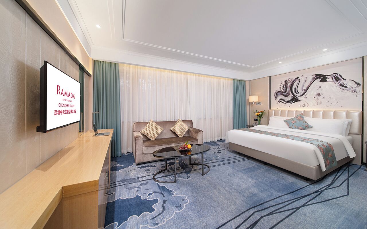A hotel room with a bed, a sofa, a coffee table, a TV, and a large abstract painting on the wall.