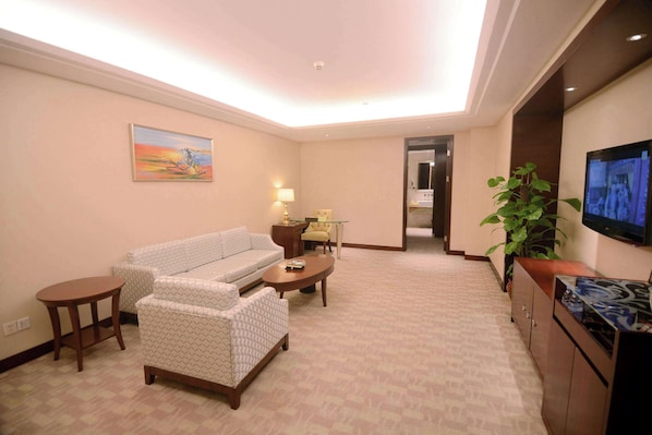 Habitación de hotel con sofá, una mesita, televisor montado en la pared y una planta.