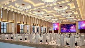 Un salón de banquetes con mesas redondas, candelabros y pantallas grandes.