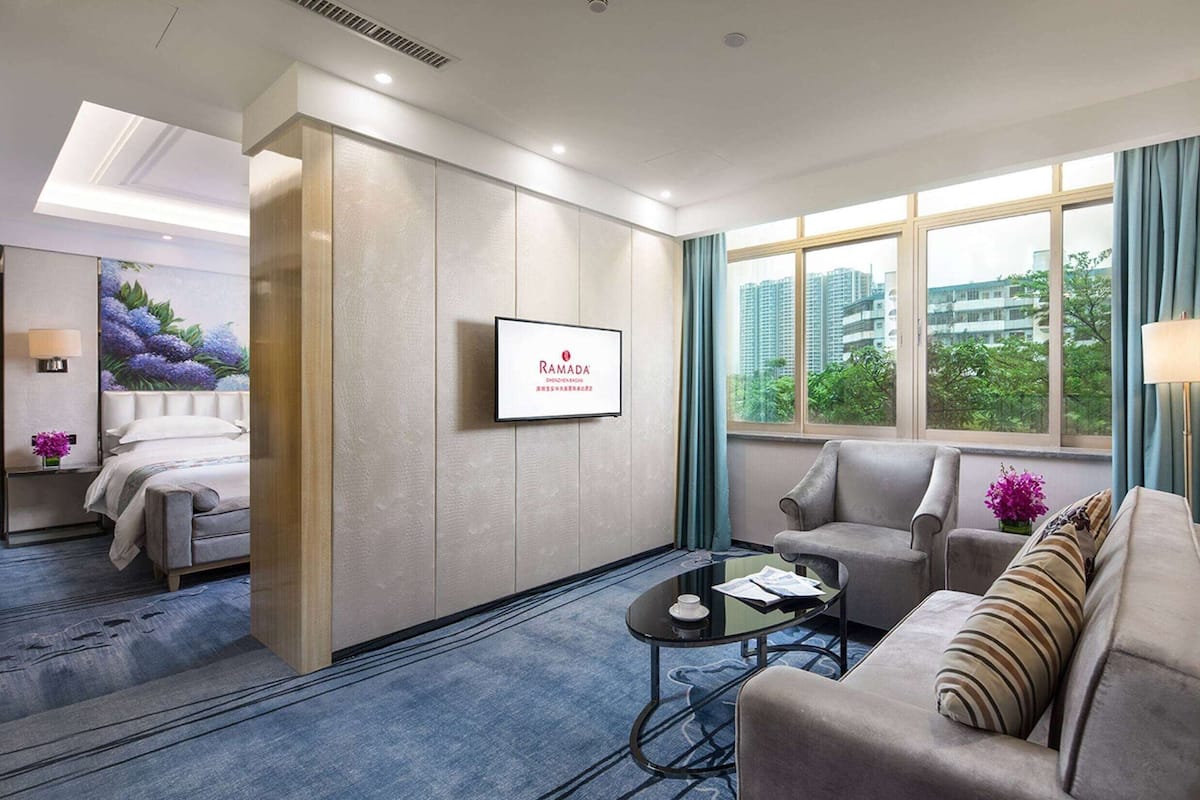 A modern hotel room with a bed, a sofa, a coffee table, and a TV.