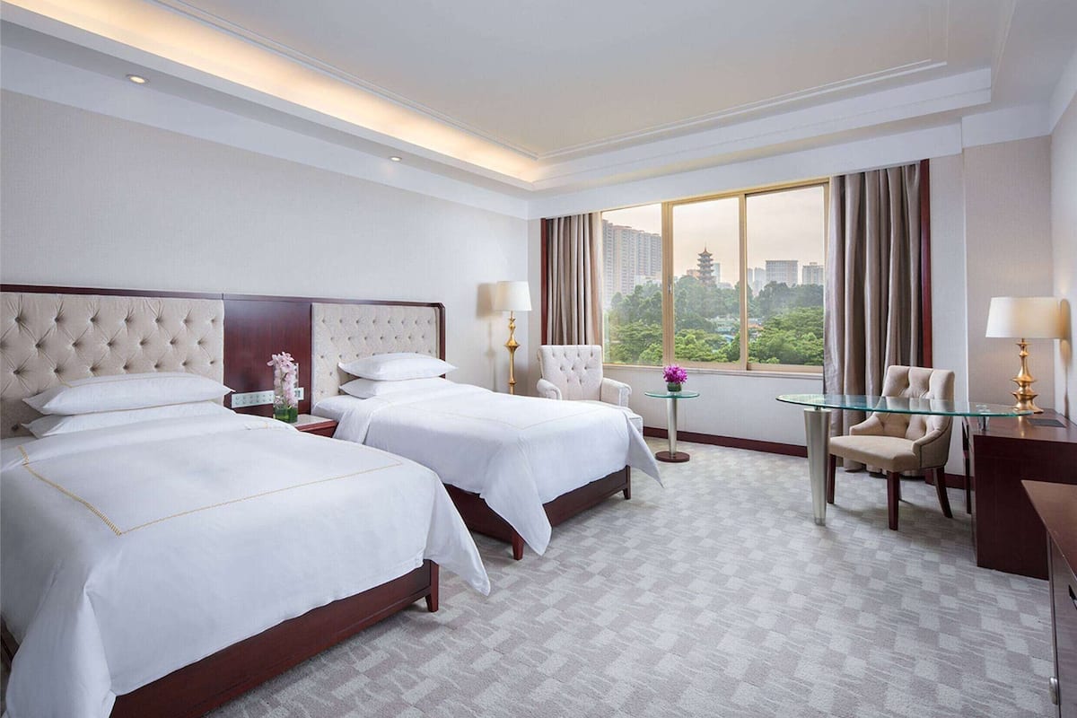 A hotel room with two beds, a sitting area with a glass table, and a view of the cityscape.