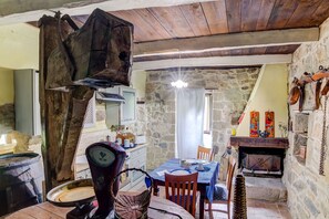 A rustic interior with a stone wall, wooden ceiling, a fireplace, and a dining table set with chairs.