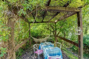 A wooden pergola with a hammock and a table set for two, surrounded by lush greenery.