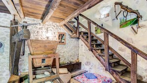 Een rustieke kamer met een houten bed, een stenen muur, een houten trap en een eenvoudige waterpomp.