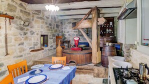 Een rustieke stenen keuken met een houten eettafel, een oude weegschaal en een traditionele fornuis.
