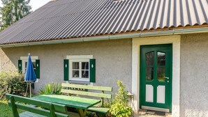 Ein Haus mit grüner Tür, einem Fenster mit Fensterläden, einer Bank und einem Tisch.