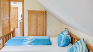 Ein Schlafzimmer mit schrägverlaufender Decke, einem Holzschrank und einem Bett mit blauer Bettwäsche.