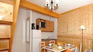 A compact kitchen with a refrigerator, microwave, and wooden cabinets. There is a dining table with chairs and a lamp. - Scenic Chalet Apartment for Groups (St. Sorlin D'arves)
