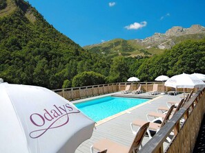 A pool area with lounge chairs and umbrellas, surrounded by a wooden deck and a mountain backdrop.