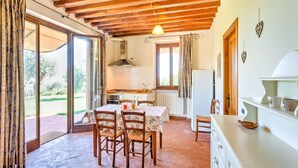 A kitchen with wooden beams, a gas stove, and a dining area with chairs and a table. - Farmhouse in Suvereto near Etruscan Coast (Suvereto)