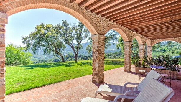A covered outdoor seating area with stone arches, a grassy lawn, and a view of trees and hills. - Farmhouse in Suvereto near Etruscan Coast (Suvereto)