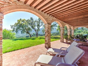 A covered outdoor seating area with stone arches, a grassy lawn, and a view of trees and hills. - Farmhouse in Suvereto near Etruscan Coast (Suvereto)