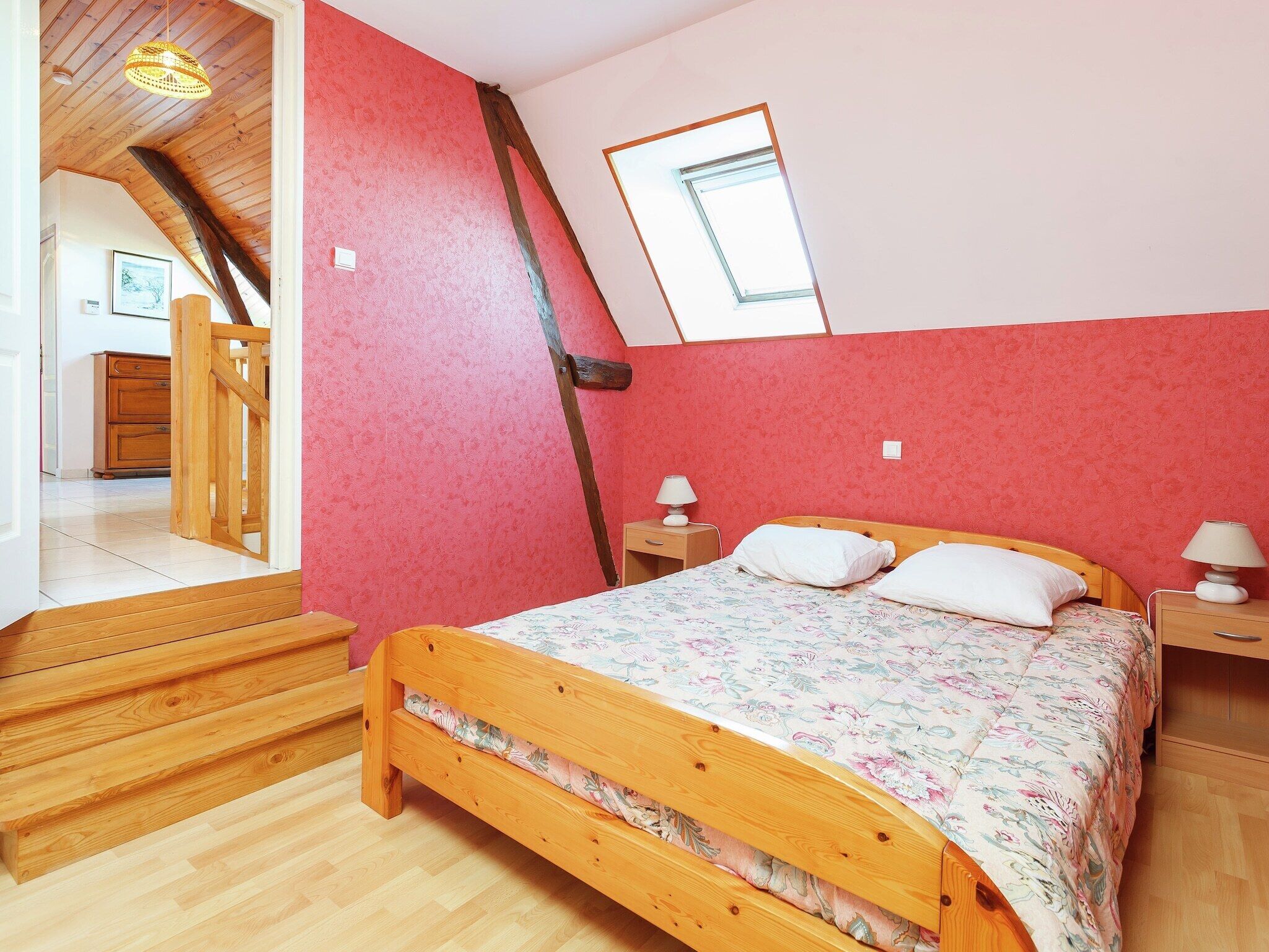 Ein Schlafzimmer mit einem Holzbett, einem Oberlicht und einer roten Wand.