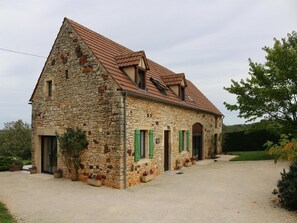 A stone building with a pitched roof, green shutters, and a gravel driveway. - Cosy holiday home near the Causses du Quercy (Lavercantiere)