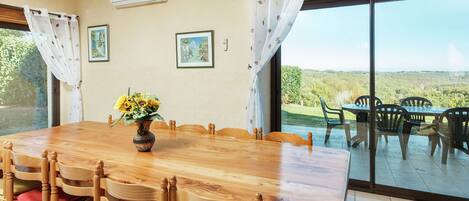 Un comedor con una mesa y sillas de madera, un jarrón con flores y vistas amplias a través de ventanas grandes.