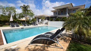 Une piscine entourée de palmiers et d’un bâtiment à toit de tuiles, avec des chaises longues et des parasols à proximité.