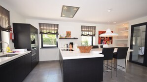Une cuisine moderne avec des meubles de couleur sombre, un îlot central, des tabourets de bar et un luminaire suspendu.