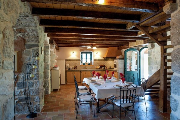 A rustic dining area with a stone wall, wooden beams, and a tiled floor.