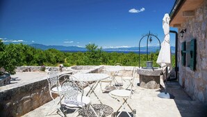 An outdoor patio with stone tables and chairs, a white umbrella, and a stone wall. - Villa on Krk with Pool and Outdoor Kitchen (Krk - Malinska)