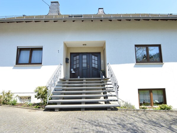 A two-story building with a dark front door, a staircase leading to the entrance, and a paved driveway.