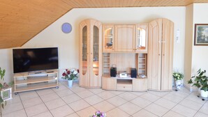 Una sala de estar moderna con un televisor de pantalla plana, armarios de madera y piso de baldosas.
