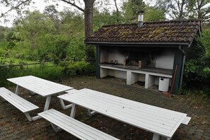 Un espace extérieur aménagé dans un style rustique, avec un foyer en pierre et entouré de verdure.