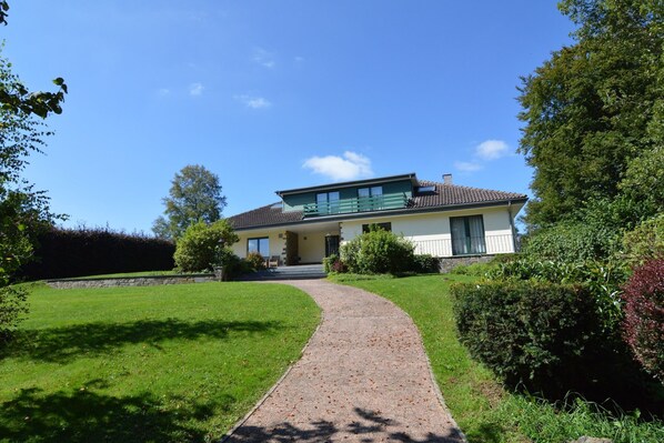 Une maison moderne avec une allée pavée menant à la porte d’entrée, entourée de pelouses et de haies bien entretenues.