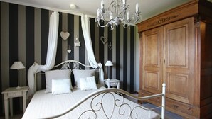 Une chambre à coucher avec un lit à baldaquin, un lustre, une armoire en bois et un papier peint à rayures.
