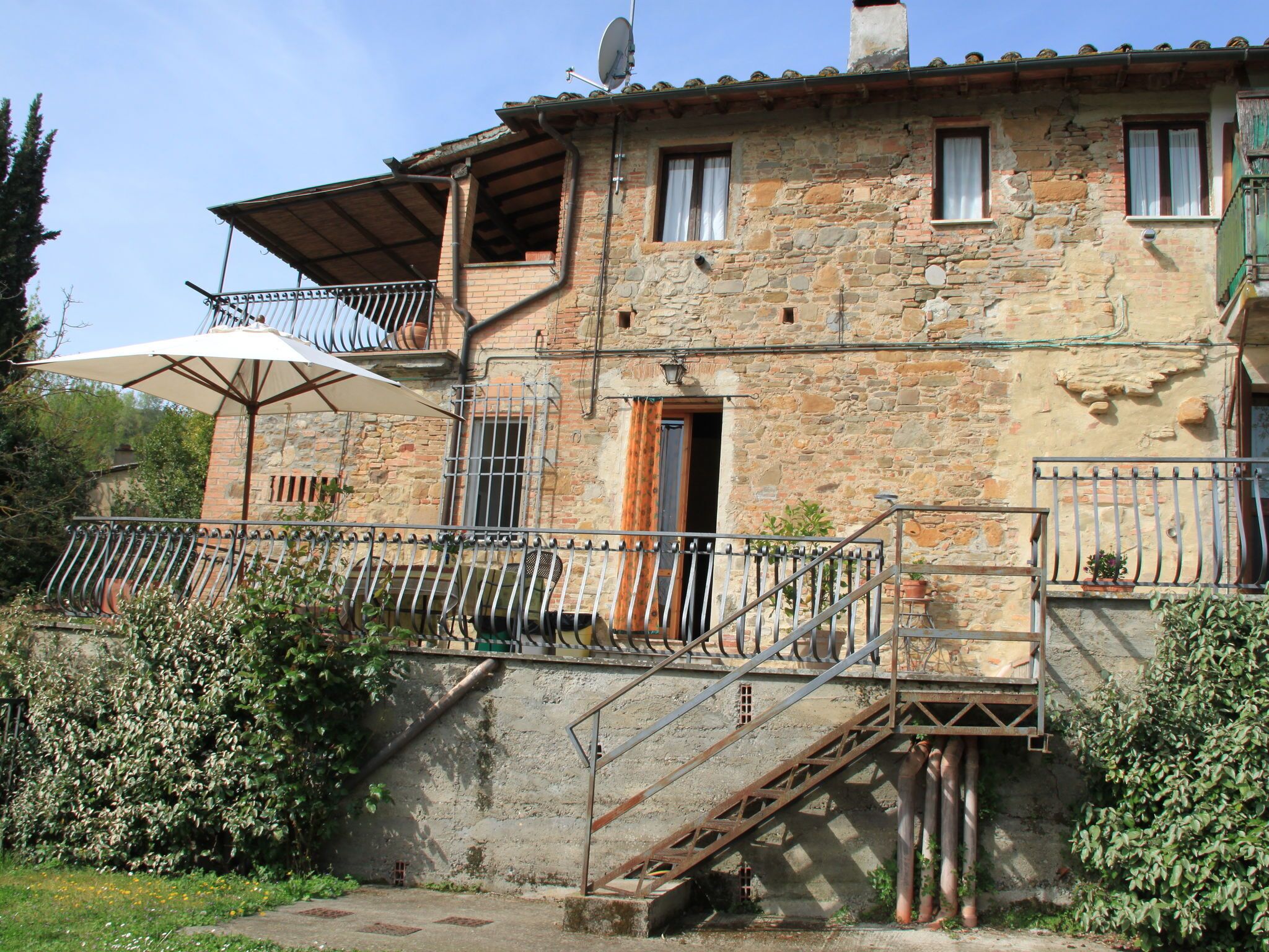 A rustic stone building with a balcony, a staircase, and a satellite dish.