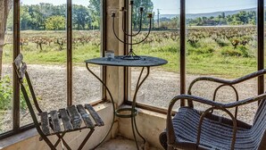 A rustic room with a large window overlooking a vineyard, a small round table with a candle, and two wicker chairs. - Cottage in Oppède amidst Vineyards (Oppède)