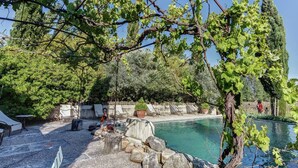 A pool area with a stone wall, seating, and a pergola with vines. - Cottage in Oppède amidst Vineyards (Oppède)