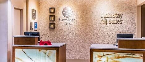 Zona de recepción de un hotel con mostradores de mármol, el logotipo de Comfort INN y la marca MainStay Suites.